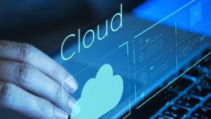 Mão feminina navegando em um laptop com um gráfico azul escrito "cloud" flutuando